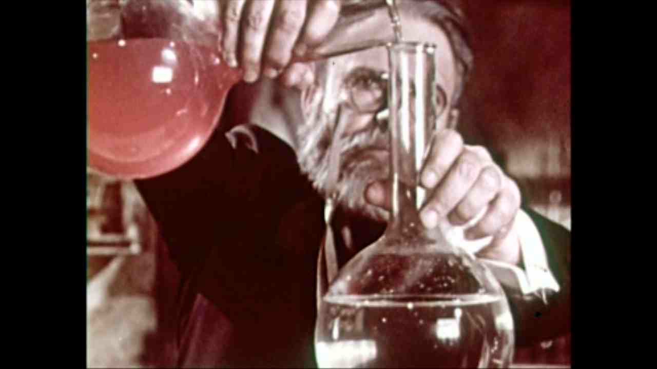 Un savant barbu observe un liquide dans une fiole, film de vulgarisation scientifique